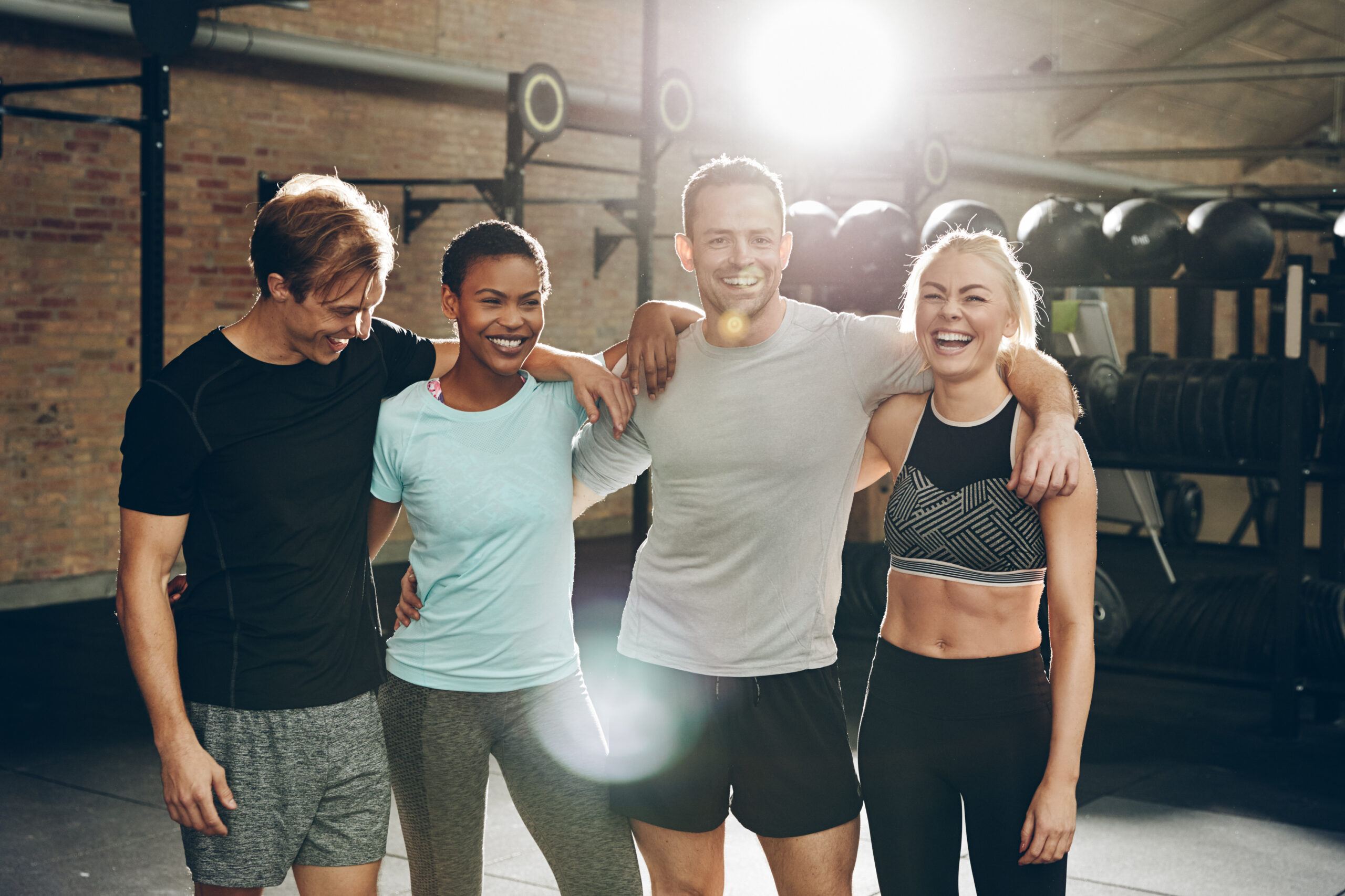 Diverse group of smiling friends in sportswear standing arm in arm together in a gym after a workout session