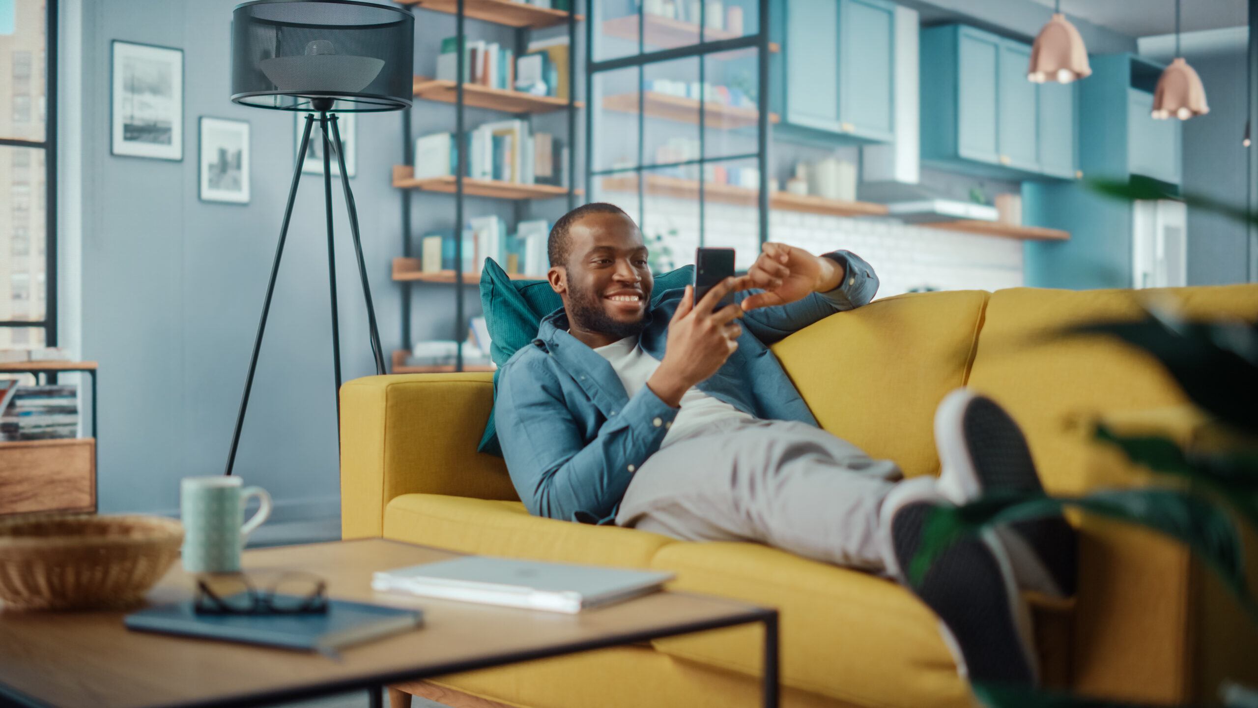 Man Using Smartphone while Resting on a Sofa in Living Room. Happy Man Smiling at Home and Chatting to Colleagues and Clients Over the Internet. Using Social Networks.